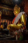 Wat Xieng Thong temple in Luang Prabang, Laos.  The main Buddha of the sim sits on a platform, surrounded by smaller statues, candles, and offerings. 